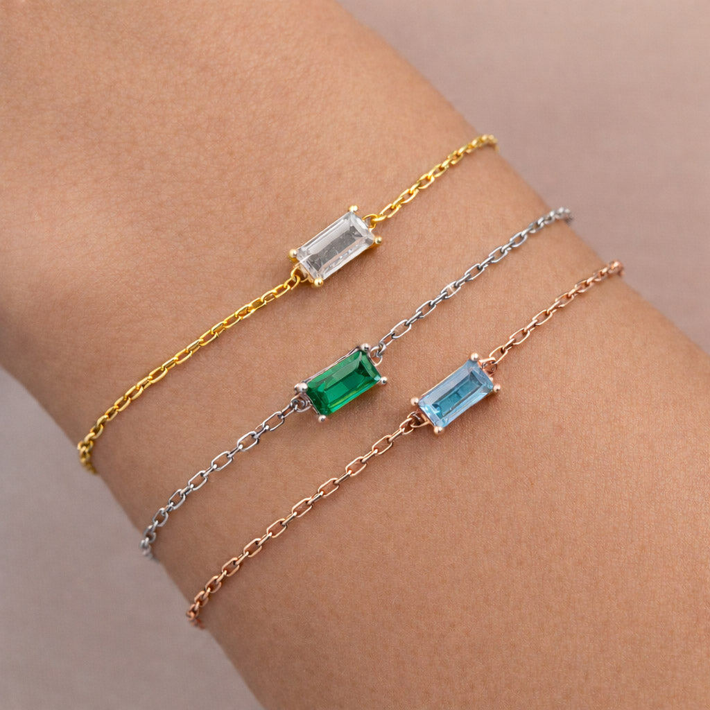 Three gold, silver, and rose gold bracelets with birthstones on a wrist.