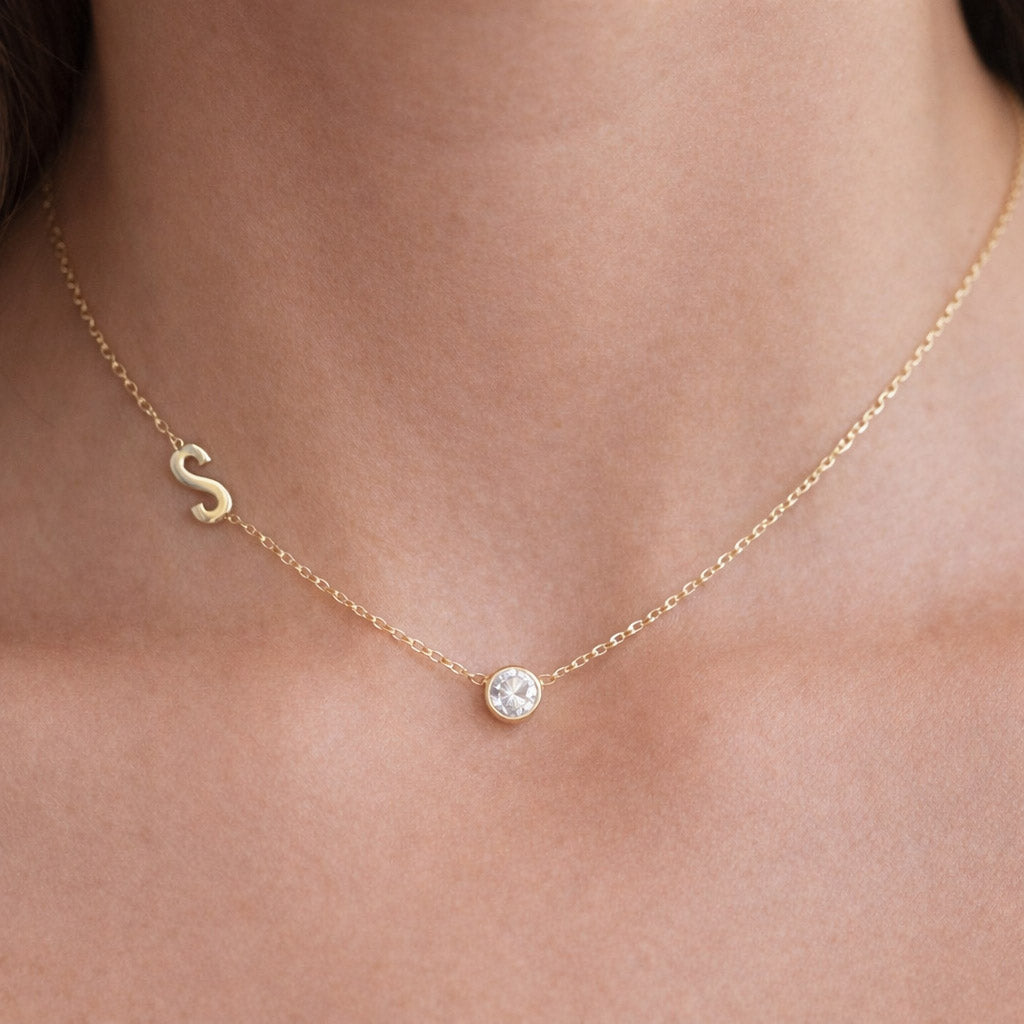 Gold necklace with personalised letter and small CZ birthstone worn by a female
