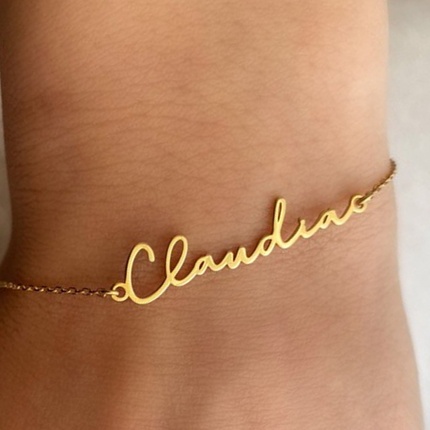 Gold name bracelet with the name 'Claudia' on a person's wrist