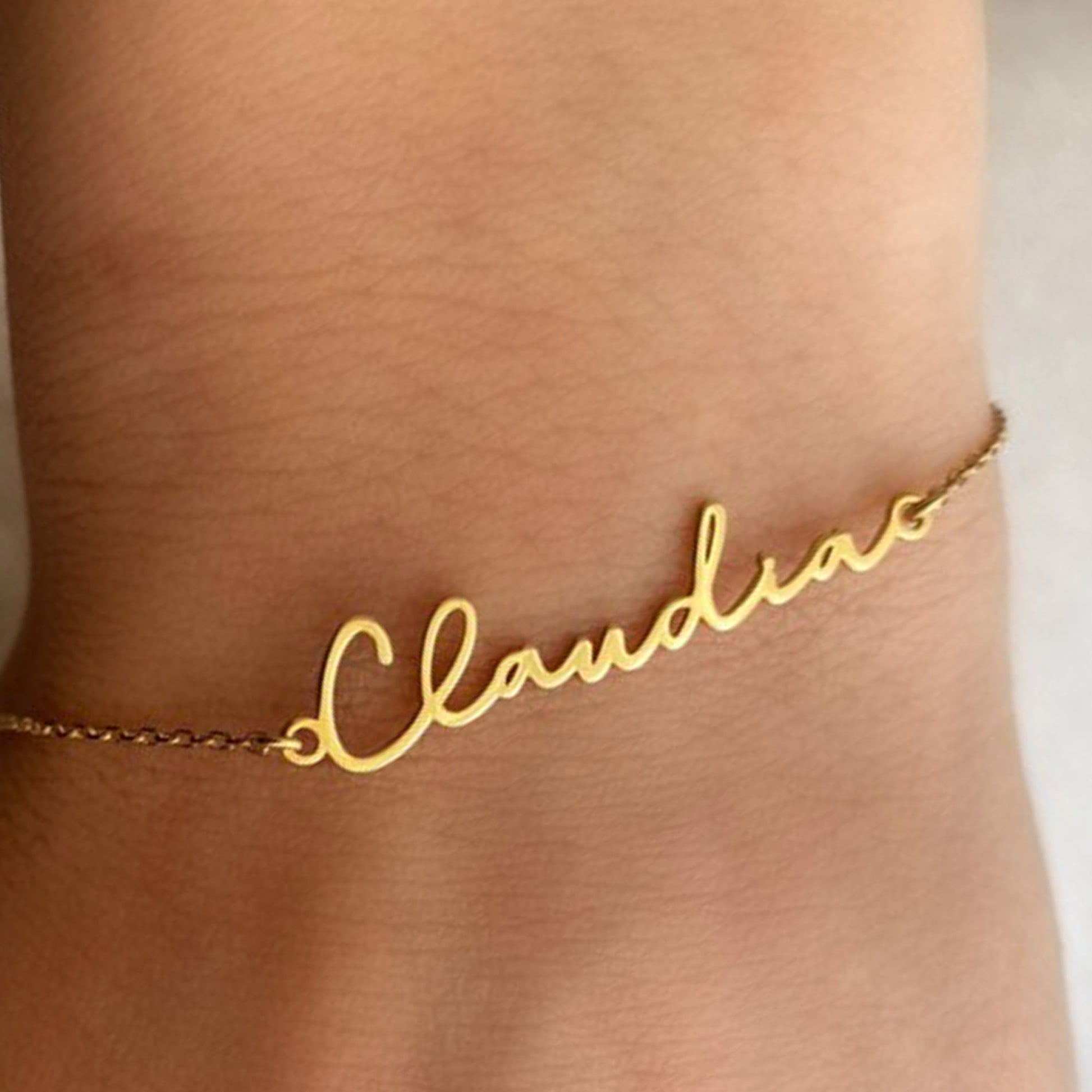 Gold name bracelet with the name 'Claudia' on a person's wrist
